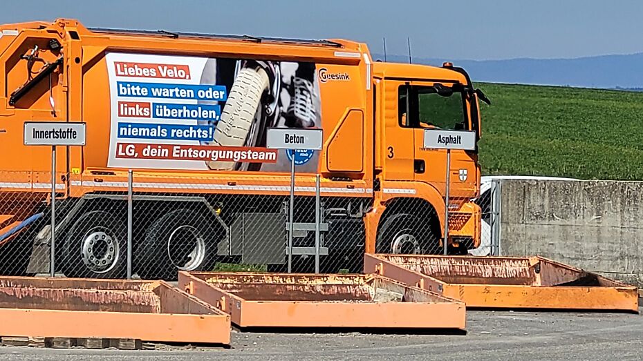 Foto eines orangen Abfallwagens der Gemeinde mit bedruckter Werbung auf der Seitenfläche des Wagens.